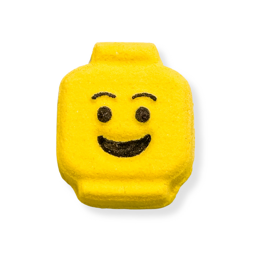 A yellow bath bomb designed to look like a smiling face, with a rectangular block shape and rounded corners.