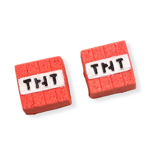 Two cube-shaped bath bombs with a red surface and 'TNT' written in white on one side, designed to look like dynamite.